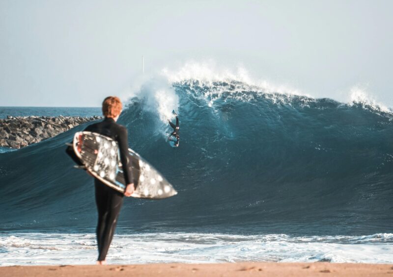 A surfer riding a big wave while another observes with a surfboard at Newport Beach, California.
